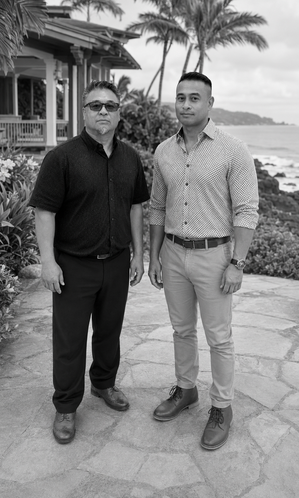 Portrait photo of two people standing on a stone path near an oceanfront home with palm trees, black-and-white, vertical composition.