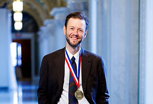 Professional image of author Mac Barnett wearing a suit and tie with the National Ambassador for Young People's Literature medal hanging from his neck