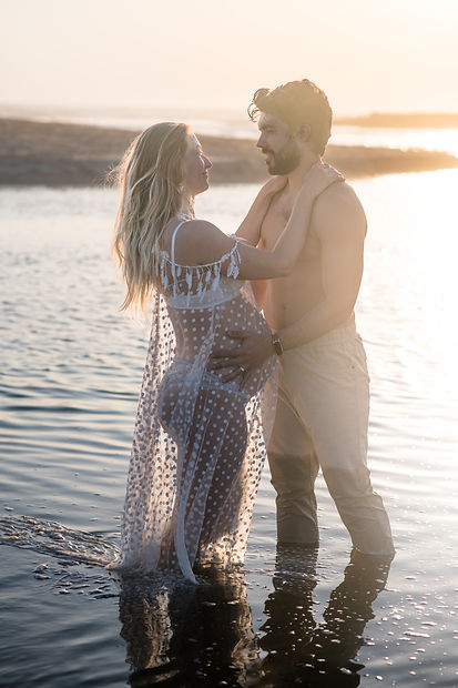 Couple attendant un enfant les pieds dans l'eau au couchant, séance grossesse dans les Landes
