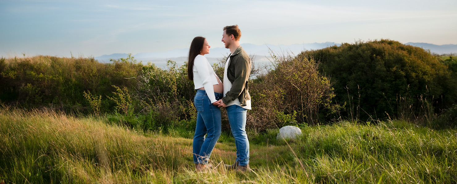 an expecting couple facing each other on a coastline