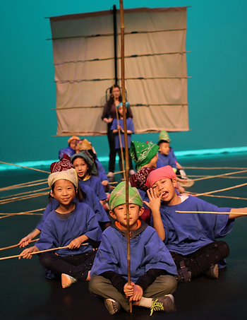children sit on a stage sailing an imaginary boat with oars and a sail