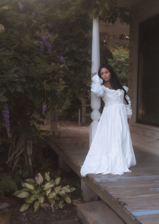 Woman in white gown leaning against porch pillar