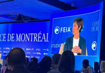 Speaker on a large blue conference screen in Montreal, with audience silhouettes and FEIA text visible.