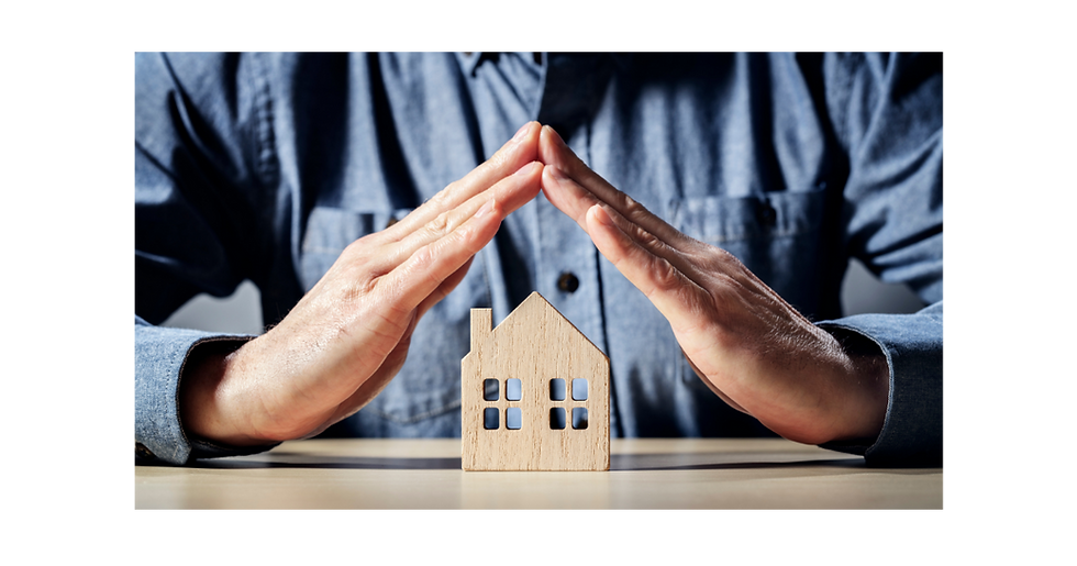 An insurance salesperson using his hands to shield a small wooden home on his desk.