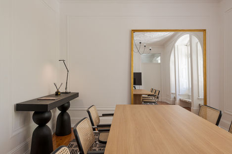 Sala de reuniões com mesa de madeira clara, cadeiras de vime e grande espelho dourado Arte Moldura, num espaço projetado pelo Atelier Rita Valadão em Lisboa.