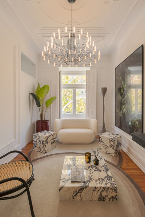 Sala de estar com sofá branco curvo, poltrona Lina Bo Bardi e mesa em mármore viola, integrada num espaço de arquitetura clássica lisboeta assinado pelo Atelier Rita Valadão.
