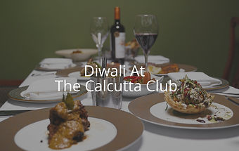 Elegant table setting with gourmet dishes, wine glasses, and a bottle on a white tablecloth. Text reads "Diwali At The Calcutta Club".