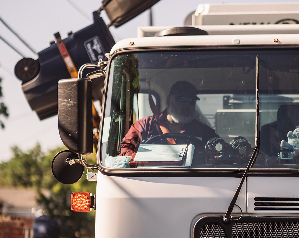 Front view of man driving waste truck and picking up garbage can
