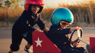 Children wearing helmets pushing each other in kart.
