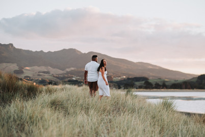 Couple walking through sand dunes in front of mountain by the beach in Raglan New Zealand on a family photoshoot