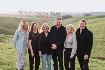 Family photo of grown up children with their parents in front of rolling hills in Raglan New Zealand.