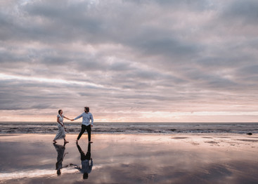 couple holding hands walking along Raglan beach at sunset after their wedding during their wedding photography