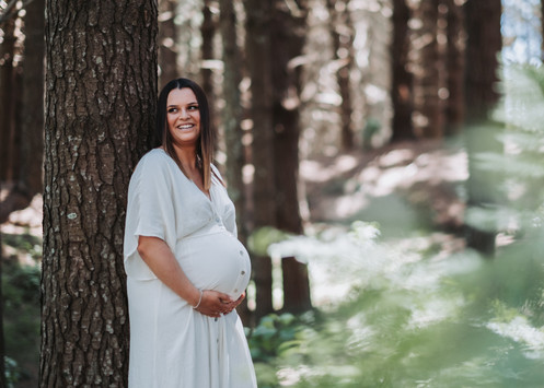 Pregnant woman leaning against a tree in Raglan pine forest for maternity photo shoot