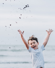 Happy child at Raglan beach throwing sand during family photos in Waikato