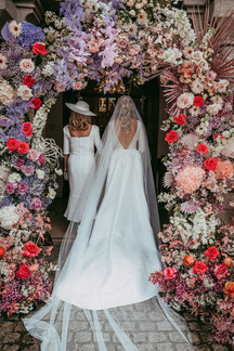 Back of bride and mother in front of door decorated with flowers.