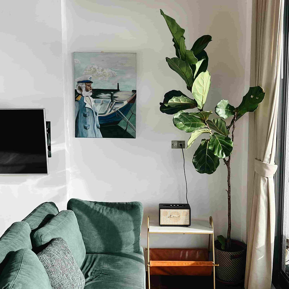 Interior de una sala de estar con un sofá verde, flores en la habitación, televisión, altavoz y cortinas, acompañado de un cuadro de un marinero con un bote en la pared.