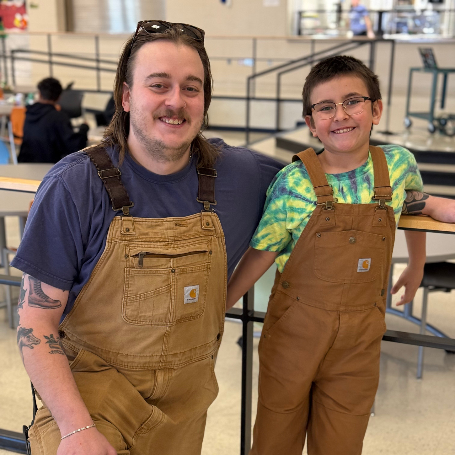student and teacher smiling at the camera wearing Carhart overalls 