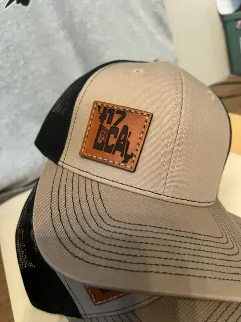 Thumbnail: Tan and black trucker hat featuring a brown leather patch with '417 Local' and Route 66 emblem, displayed with a matching cap