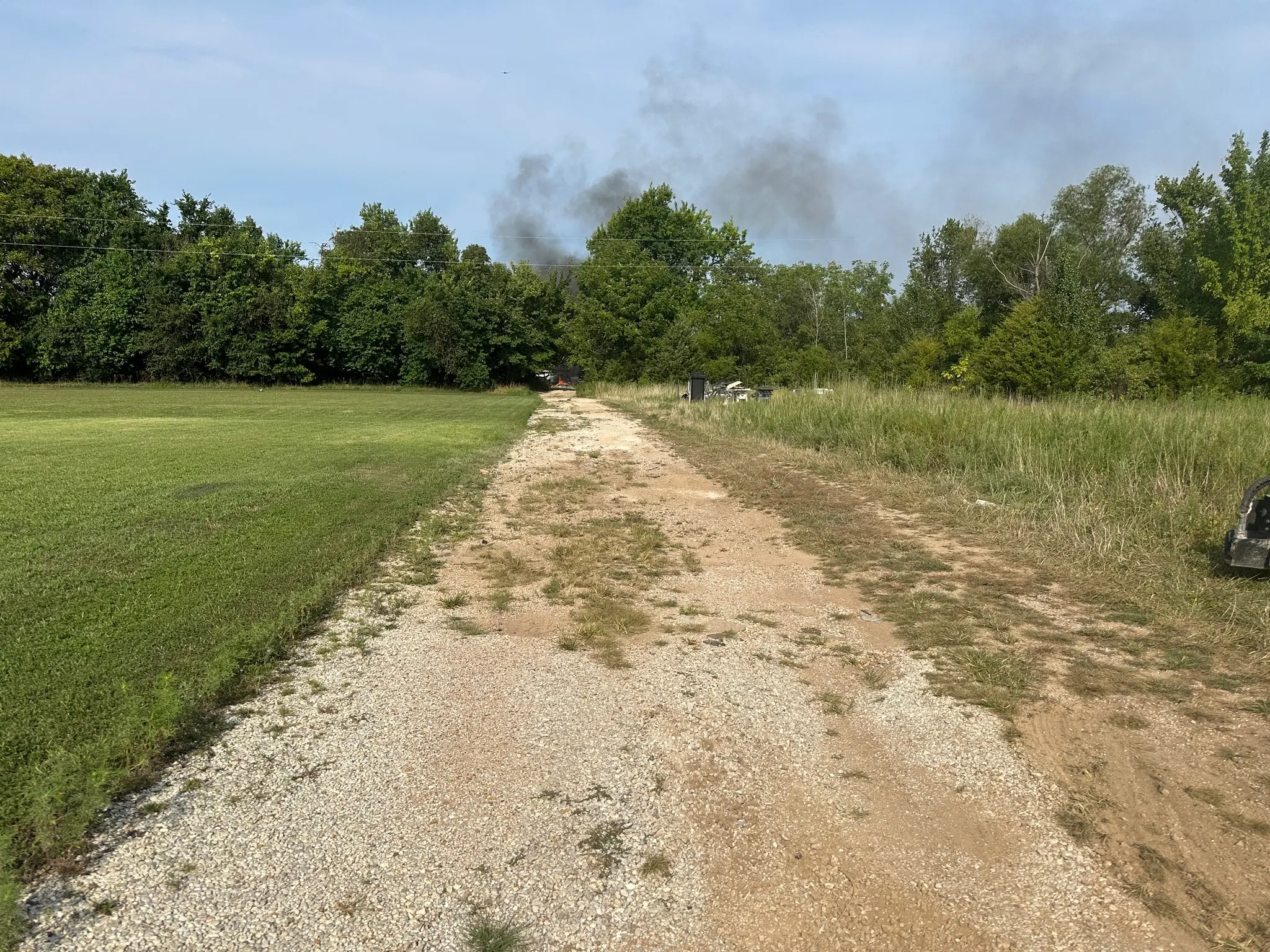 Worn rural gravel driveway with exposed dirt, thin gravel coverage, ruts, and uneven washed-out areas before repair