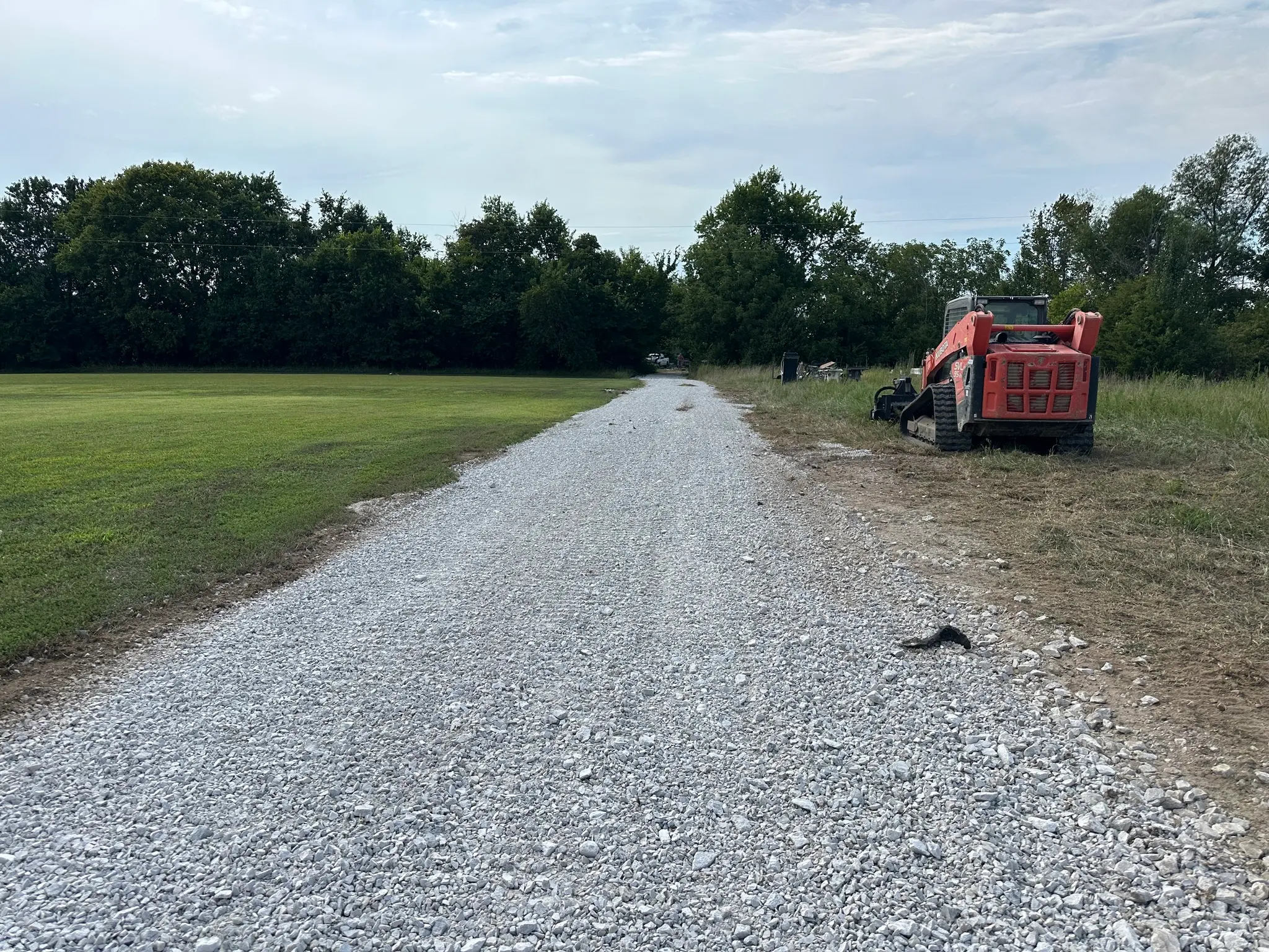 Fresh gravel spread and graded across a rural driveway with a skid steer parked beside the finished surface