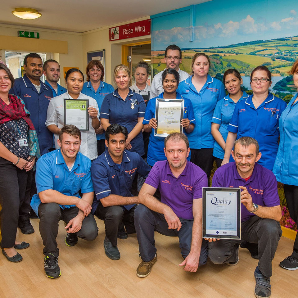 Group of proud care staff pose with awards in reception of a care home
