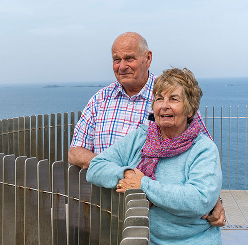 Couple pose looking out over the sea.