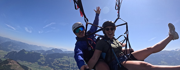 Zwei Menschen beim Gleitschirmfliegen über Bergen