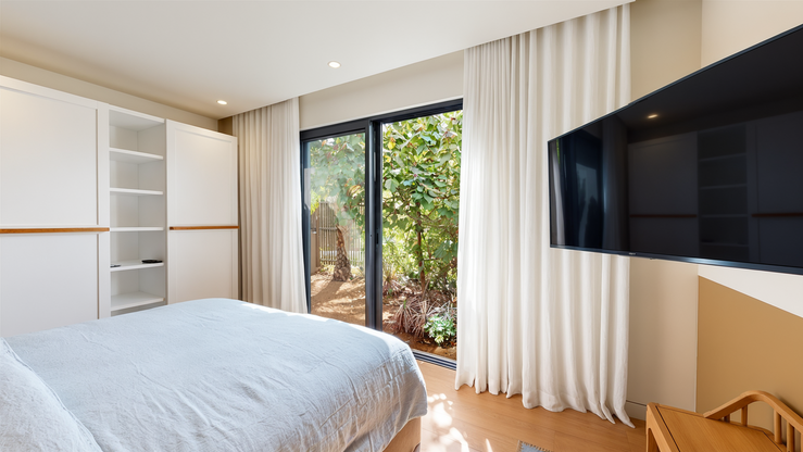 Chambre avec lit double, rangements intégrés, télévision et baie vitrée ouverte sur la végétation tropicale