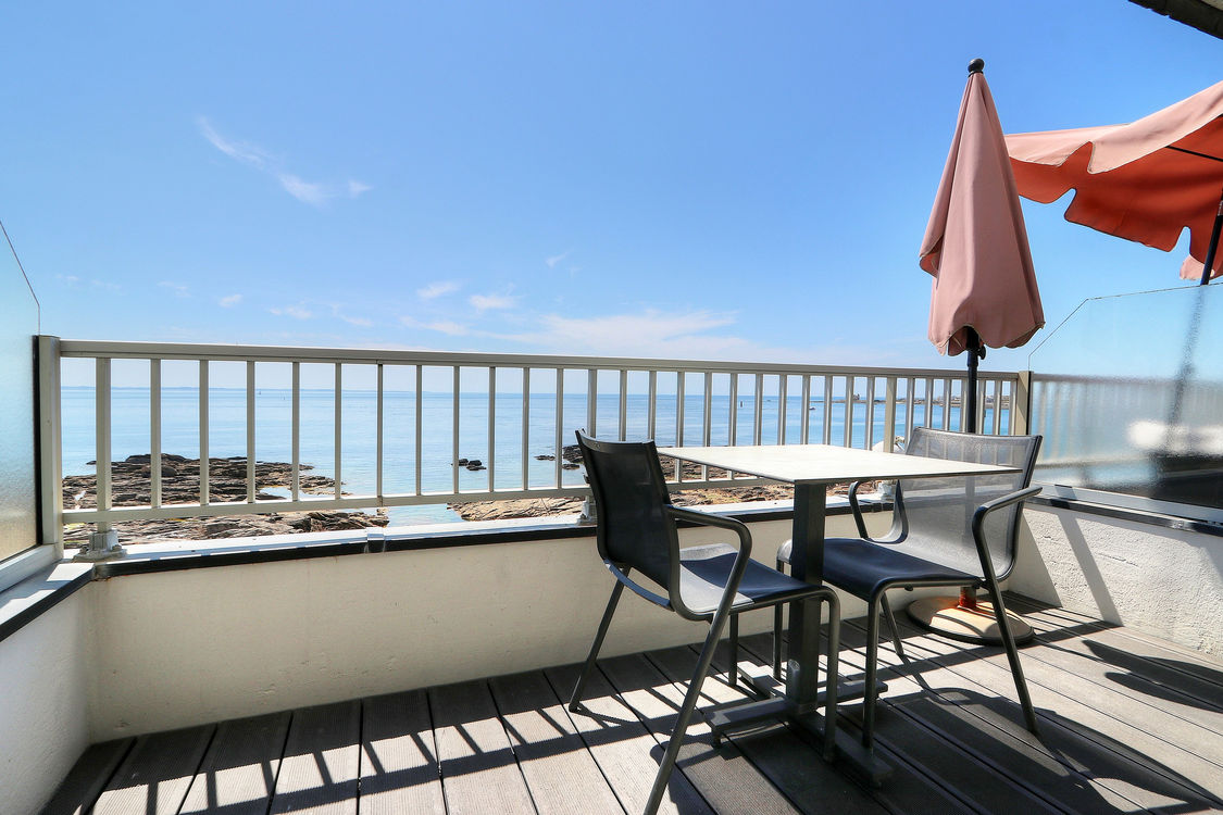 Terrasse avec table, chaises, parasol et vue sur la mer.