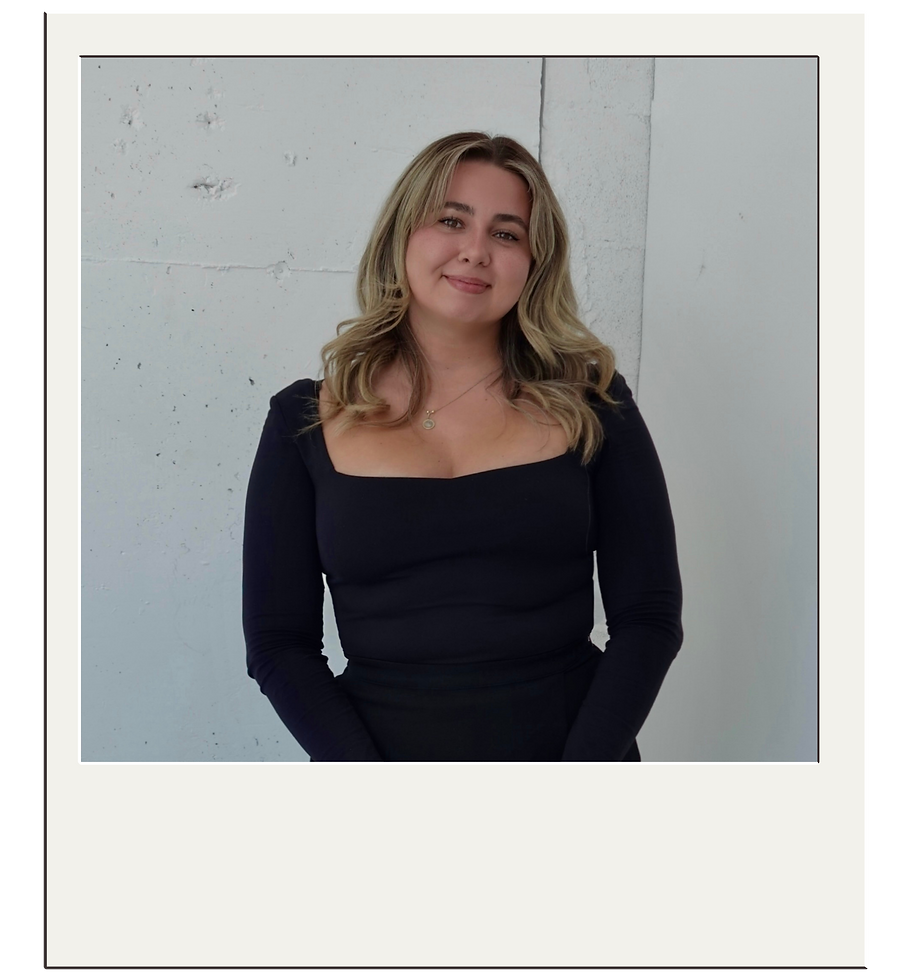 Portrait of a woman smiling in a black top, posed against a minimal white textured wall in a polaroid-style frame.