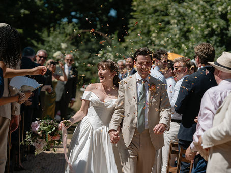 A happy newly married couple walking inbetween guests at a garden wedding with confetti being thrown