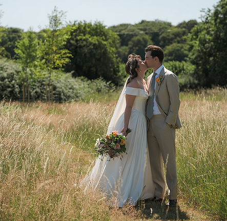 Bride and groom kissing in meadow of long grass