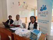 Naomi Chepkemoi from Hesed World and JKUAT tournament organizers at the registration booth, with branded materials including t-shirts, notebooks, and a banner displaying 'Generations united. Change ignited