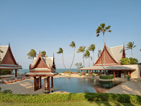 Sunny tropical resort with Thai-style pavilions, palm trees, and a pool beside the sea, calm and empty.