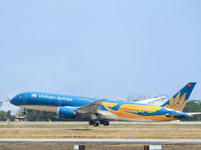 Vietnam Airlines plane taking off from a runway. Blue sky and cityscape in background. The aircraft is blue and yellow with visible logos.