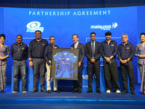 Eight people smiling, holding a framed jersey on stage. Blue background with text “Partnership Agreement,” logos of Mumbai Indians and Malaysia Airlines.