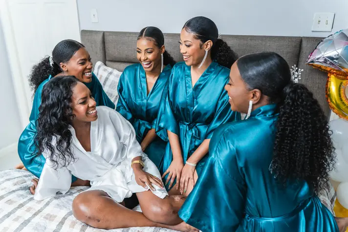 Bride and her bridesmaids dressed in robes share a fun moment on a bed as they get ready.