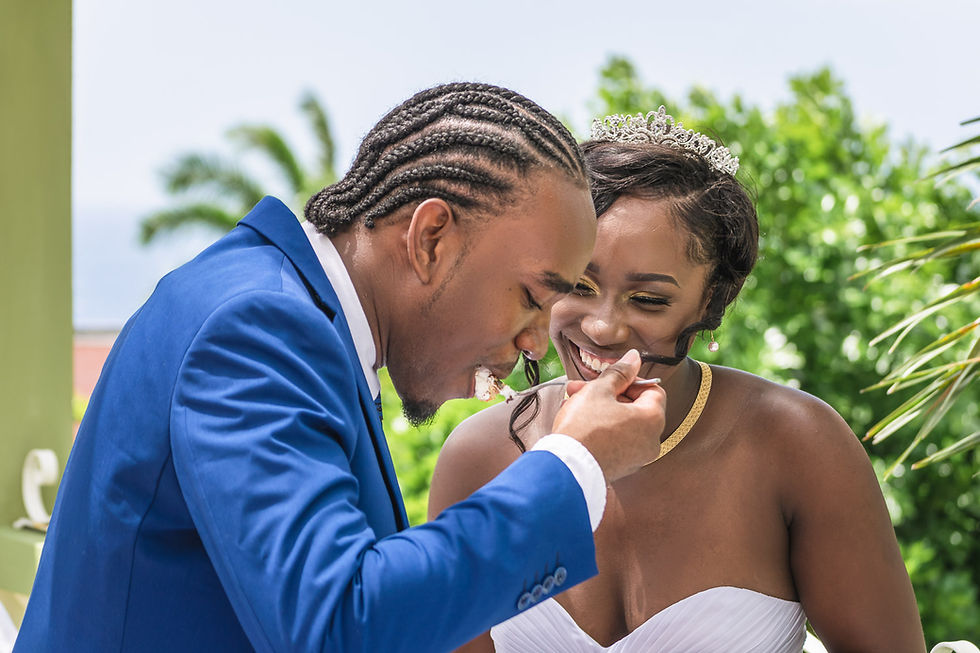 Bride smiles as her groom takes a bite of their wedding cake.