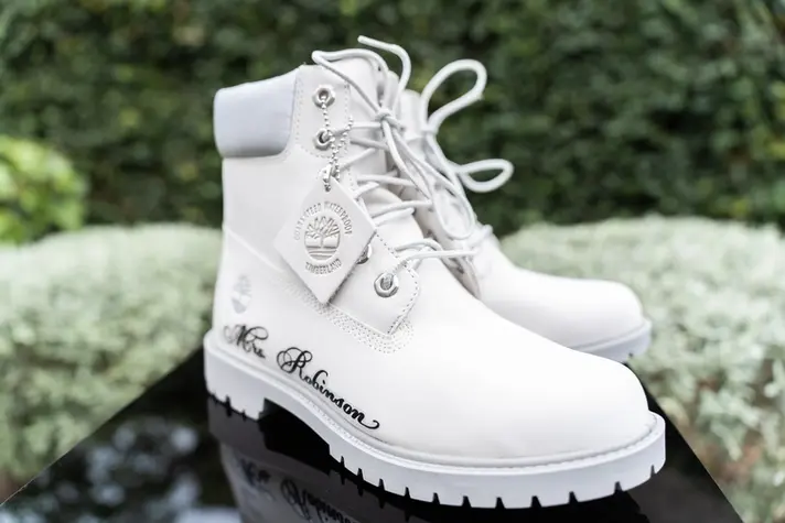 Brides white timberland boots with her name inscribed, photographed on reflective black acrylic sheet