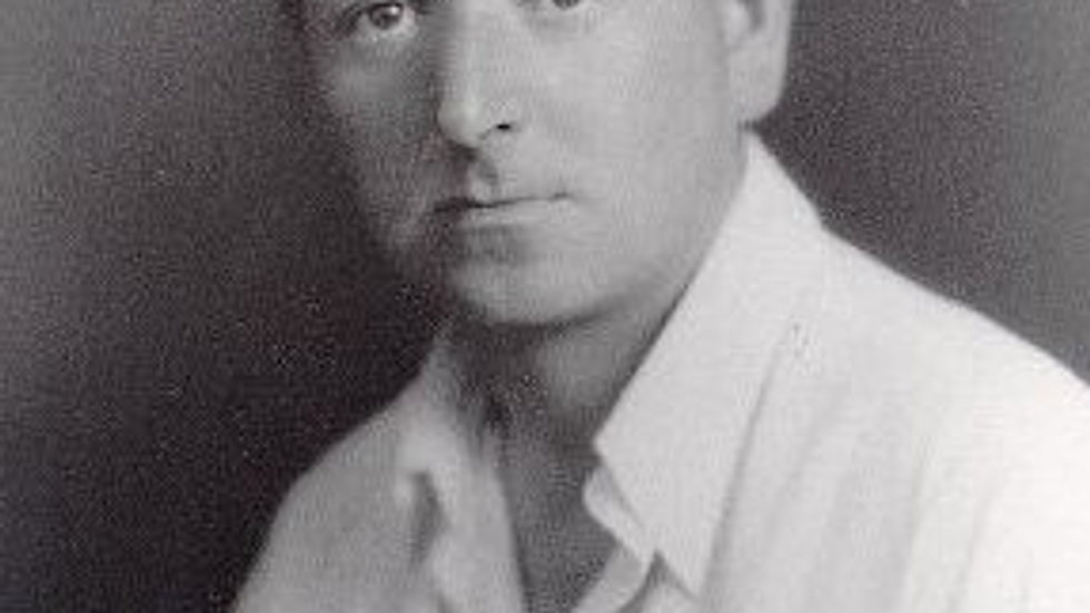 Black and white portrait of a man in a white shirt, looking at the camera with a neutral expression. Plain dark background.