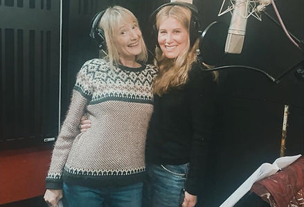 Virginia Byron and fellow actor smiling to camera in a sound recording studio infront of microphone and wearing headphones