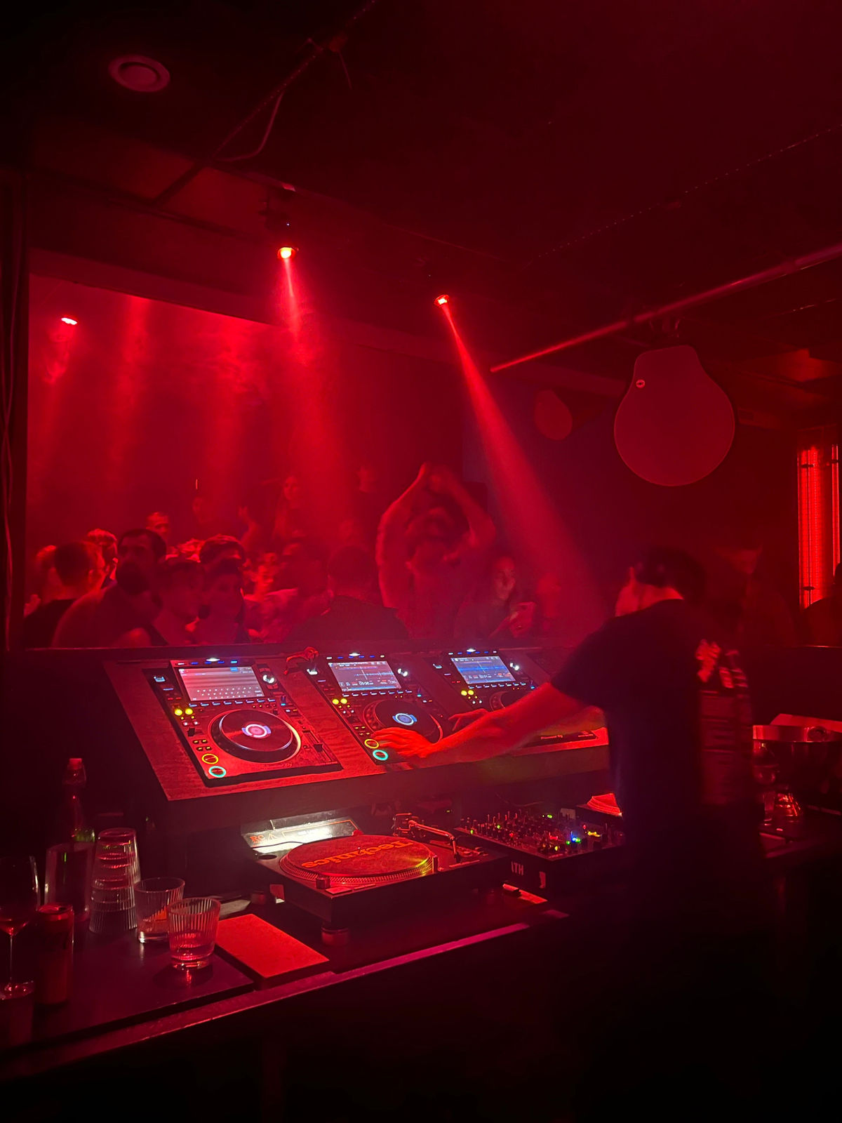 DJ at the decks in front of a dancing crowd under red light