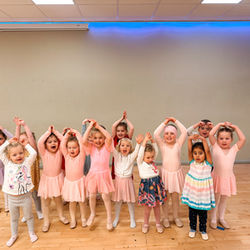 Young ballerinas wearing pink tutus and leotards pose for a group photo.