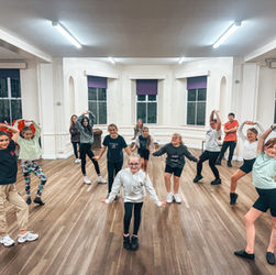Young dancers pose in a dance studio with arms raised for class.