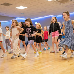 Young dancers practice choreography in a dance studio with wooden floors.