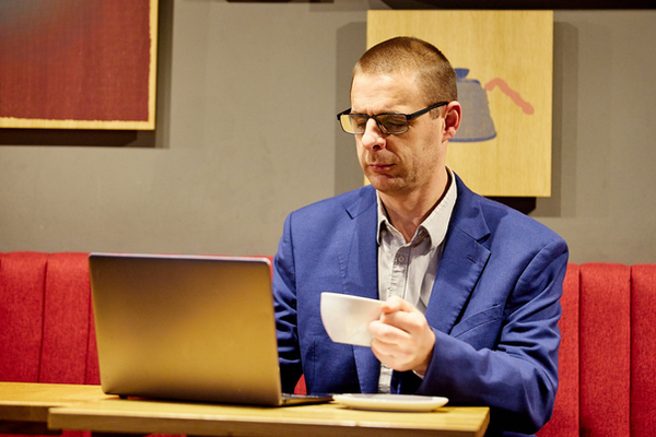 Joel White drinking coffee whilst using laptop, resources for men who need additional support including crisis lines and helplines