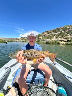 Client in a drift boat smiling while holding a trout on a San Juan River fly fishing trip.