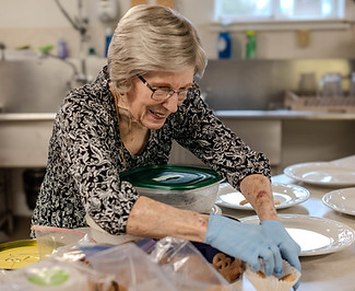 Smiling woman preparing plates of cookies in a commercial kitchen.