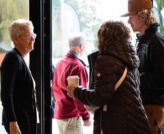 Smiling woman greeting people near church entrance doors.