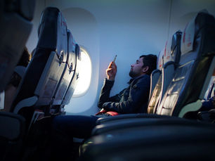 Passenger using a smartphone while seated inside a commercial aircraft cabin.